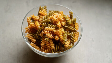 Bowl filled with colorful fusilli pasta on a light gray surface under natural light
