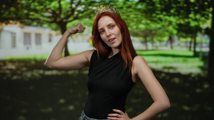 Woman flexing muscles wearing crown in sunlit park showcasing strength and confidence with a...