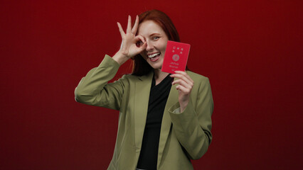 Woman posing with japanese passport against red background, making ok gesture with hand, showcasing...