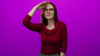 Redhead woman gazing into the distance against an isolated vivid pink background, wearing glasses...