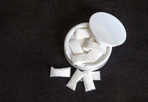 white container of small nicotine pouches on a solid black background with copy space