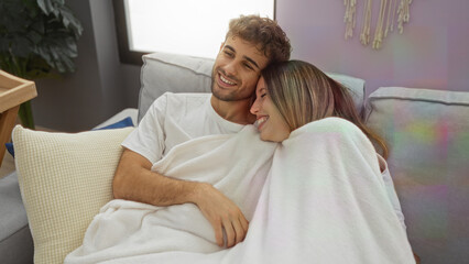 Obraz premium Couple relaxing on sofa under blanket in cozy living room showcasing love, warmth, relationship, and comfort during a peaceful indoor afternoon.