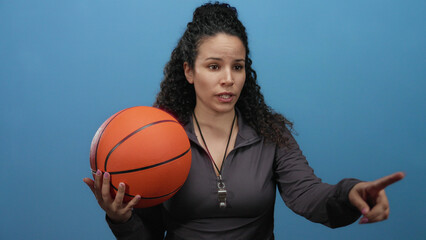Woman coach holding basketball and pointing against blue wall with determined expression on...