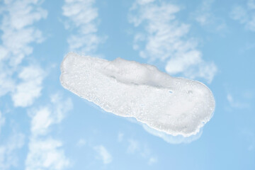 Smear of facial cleansing foam against background of blue sky and clouds.