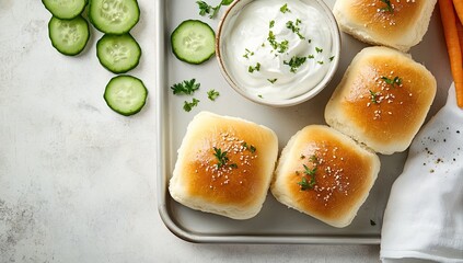 Square dinner rolls, topped with seasonings, served with cucumber slices and a dollop of creamy sauce