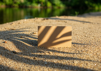 Kraft paper card with palm leaf shadows on sandy beach surface