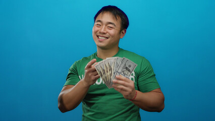Man smiling holding dollar bills against blue background showcasing success and happiness.
