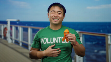 Young man wearing volunteer shirt holds orange ribbon on cruise ship with ocean background...