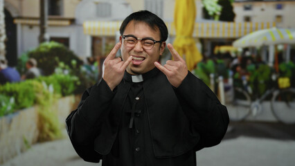 Asian man wearing priest outfit stands smiling in outdoor cafe with vibrant urban background,...
