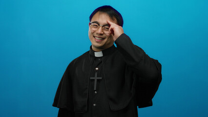 Man wearing priest attire posing against blue background confidently indicates a calming religious...