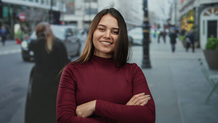 Woman with crossed arms smiles confidently on a busy urban street, blending modern style with...