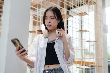 Young asian woman using smartphone and holding headphones in modern office