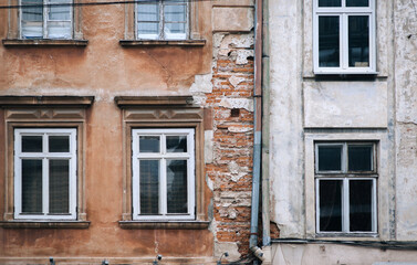 An old building with windows and a drainpipe is in a state of decay, revealing red bricks from...