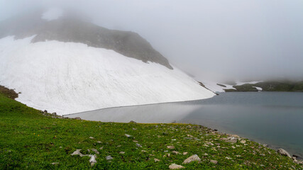 Glacial lake in low clouds in foggy changeable weather