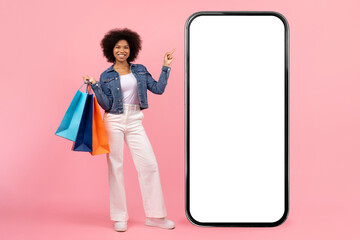 Online Shopping App. Happy young black woman pointing at big smartphone with blank white screen and...