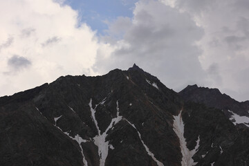 Jagged Dark Rock Mountain Peak With Streaks Of Snow, Against A Dramatic Cloudy Sky. Alpine Scenery.
