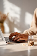Fototapeta premium Young man focused on laptop near jar of capsules in daylight minimalist interior, creative calm vibe, Selective Focus..