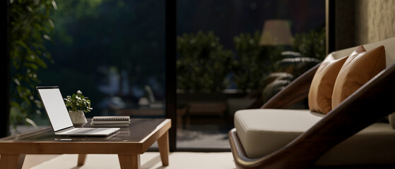 White screen laptop on table in front of a sofa or armchair in living room with glass door at night.