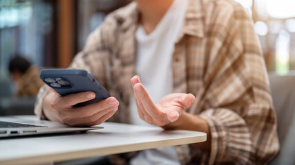 Close up of a man hands holding phone over laptop and talking or explaining sitting at cafe's table.