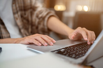 Close up of man hands typing and tapping on laptop with phone and notebook aside sits at cafe table.