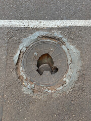 Damaged manhole cover or access cover on the road. Danger zone. Cast-iron access cover with damage. Inspection hatch poses danger to vehicles and pedestrians