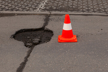 Road hazard: traffic cone marking deep pothole. Damaged asphalt with safety cone as warning sign. Road maintenance issue.