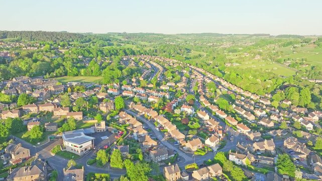 Aerial footage of Matlock Sparrow Park, Derbyshire, England, shows curving residential streets among dense trees and rolling hills, illustrating harmonious village design and lush countryside