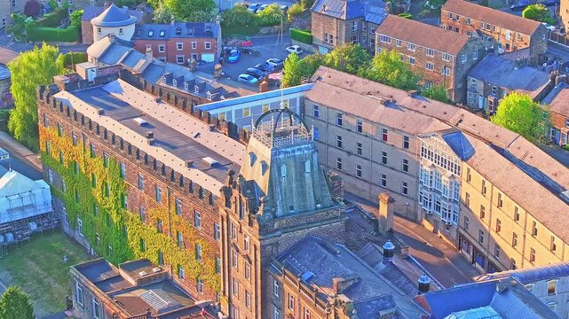 Drone orbits the grand Victorian-era country hall building at Matlock Sparrow Park, Derbyshire, England, featuring ivy-clad walls, ornate tower, and large windows, surrounded by stone townhouses,