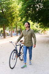 Obraz premium Young man walking with his bicycle in a city park enjoying a sunny day