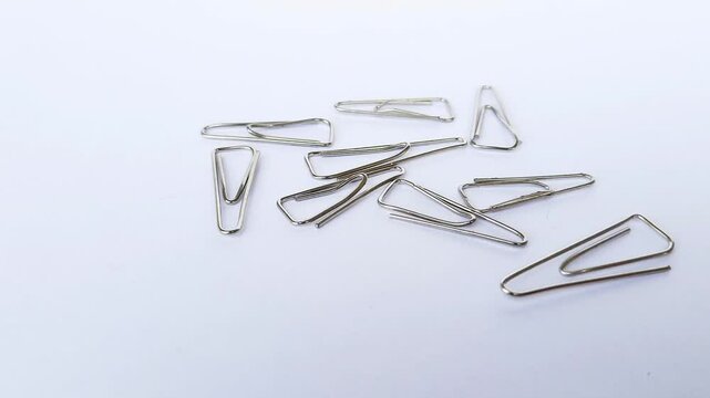 Scattered trigonal-shaped metal paper clips, isolated on a white background. Office and stationery supplies concept