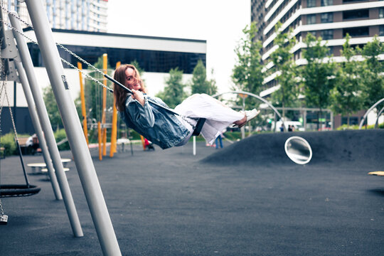 Young happy caucasian woman having fun on a swing at the playground in the city