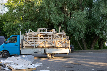 Old blue truck loaded with wooden pallets and construction debris on city street near trees.