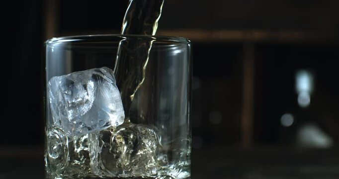 Super Slow Motion Close Up of Crystal Clear Ice Cubes in a Glass with Cold Liquid Pouring. Refreshing Beverage Preparation with Bokeh Background in Elegant Lighting 1000 fps.