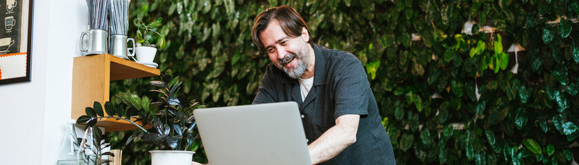 Cheerful cafe owner chats with a financial advisor via video call at his cozy coffee shop. Surrounded by greenery, he discusses business strategies and growth opportunities with enthusiasm.