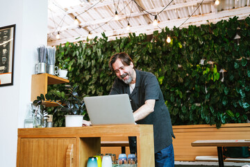 Cheerful cafe owner chats with a financial advisor via video call at his cozy coffee shop. Surrounded by greenery, he discusses business strategies and growth opportunities with enthusiasm.