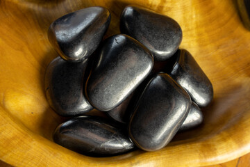 Bowl of black rocks sits on a wooden table. The rocks are all different sizes and shapes, but they...