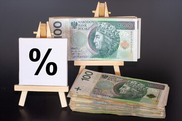 100 Polish zloty (PLN) banknotes next to a percentage sign displayed on miniature easels, symbolizing interest rates, inflation, or financial growth – conceptual finance image.