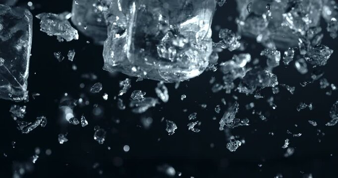 Super Slow Motion Close Up of Flying Ice Cubes with Splashes and Shards on a Dark Blue Background. Frozen Crystals Suspended in Air, Refreshing Cold Beverage Cocktails at 1000 fps. 