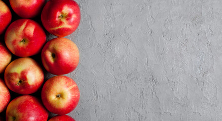 A row of vibrant red apples lines the left side of a textured light gray plaster background. Minimalist design. Copy space. Banner