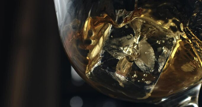 Super Slow Motion Close Up of Crystal Clear Ice Cubes in a Glass with Cold Liquid Pouring. Refreshing Beverage Preparation with Bokeh Background in Elegant Lighting 1000 fps.
