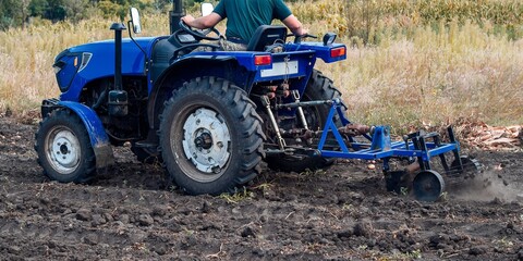 A farmer drives a blue tractor, expertly tilling the rich soil to prepare the field for planting.
