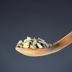Whole cardamom seeds in natural wood spoon, ideal for aromatic seasoning and exotic recipe...
