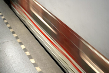 Blurred motion capture of a subway train passing by at a station platform, emphasizing speed and...