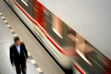 Blurred motion of a businessman walking on a subway platform alongside a passing train,...