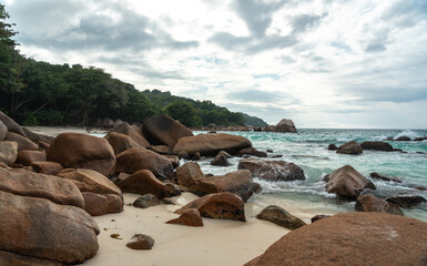Tropical coast with large rocks, turquoise sea, sandy shore, tree branch and distant islands