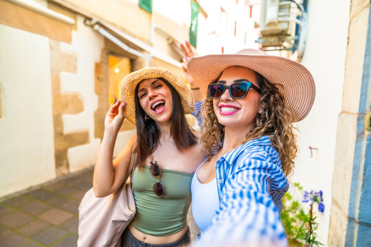 Two happy tourists taking a selfie while walking down a narrow street in summer