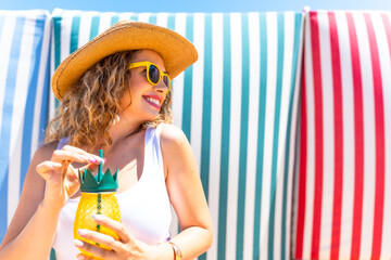 Tourist enjoying pineapple cocktail on a sunny beach with colorful striped background