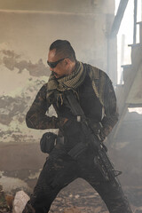 Portrait of infantryman in camouflage military uniform standing with rifle in hands in abandoned demolished building.
