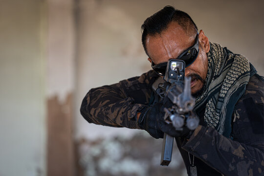 Portrait of infantryman in camouflage military uniform standing with rifle in hands and looking at camera while standing in abandoned demolished building. - Powered by Adobe