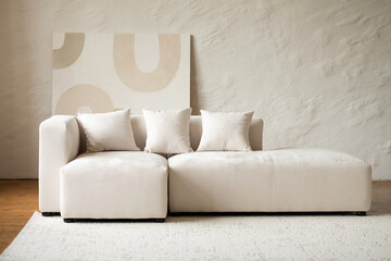 White modern beige sectional sofa with cushions and abstract art on wall. Contemporary minimalist interior design for living room or studio.